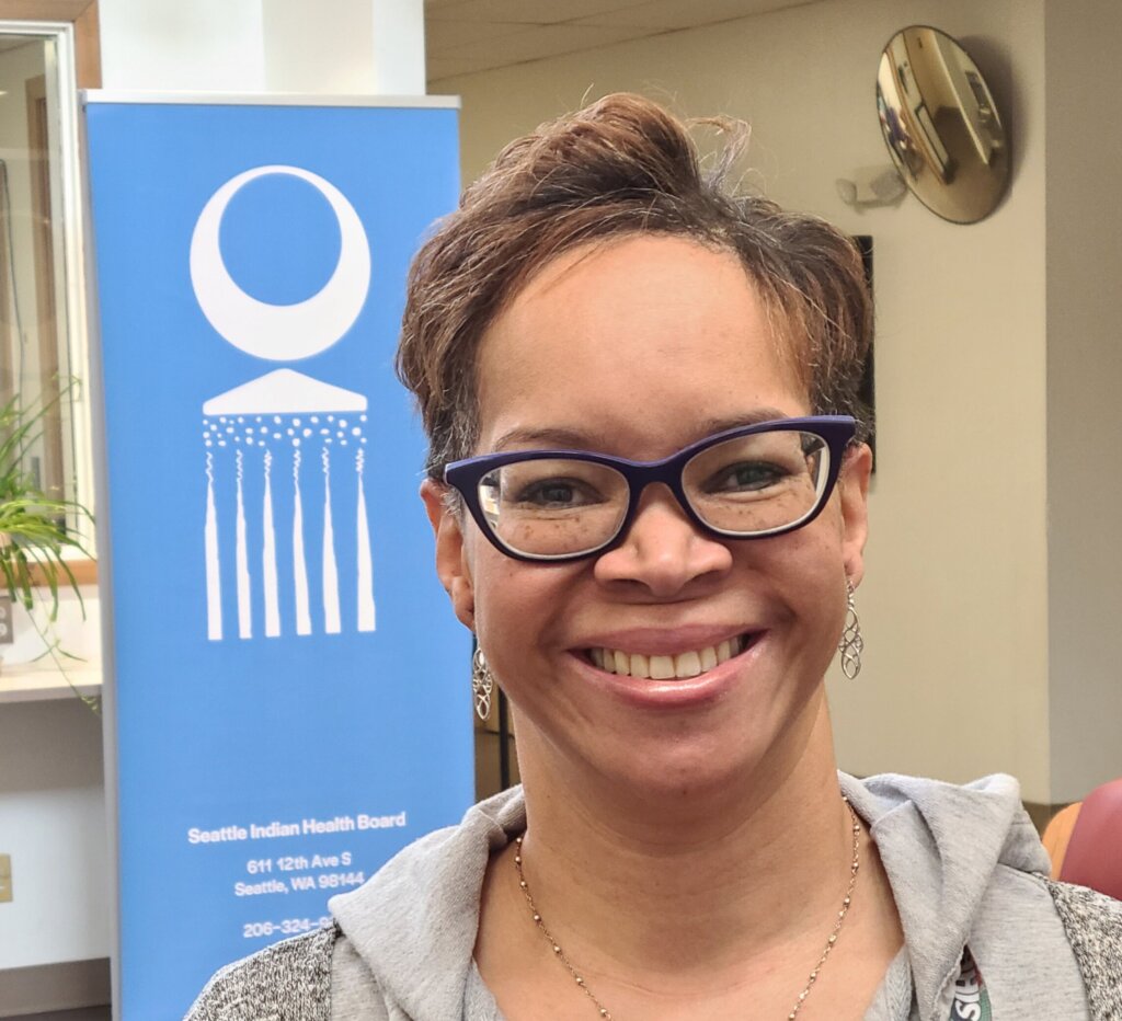 Portrait of pharmacy director Terri Adams-Kincaid, in front of poster featuring SIHB logo