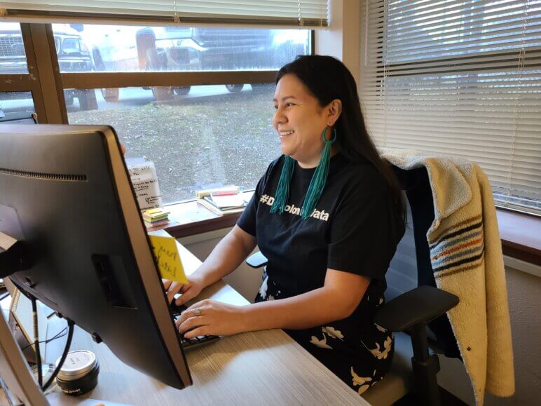 A smiling woman wearing long leather earrings is typing in an office.